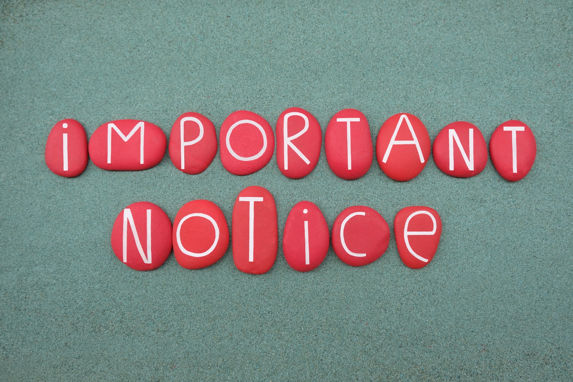 Important notice text composed with red colored stone letters over green sand